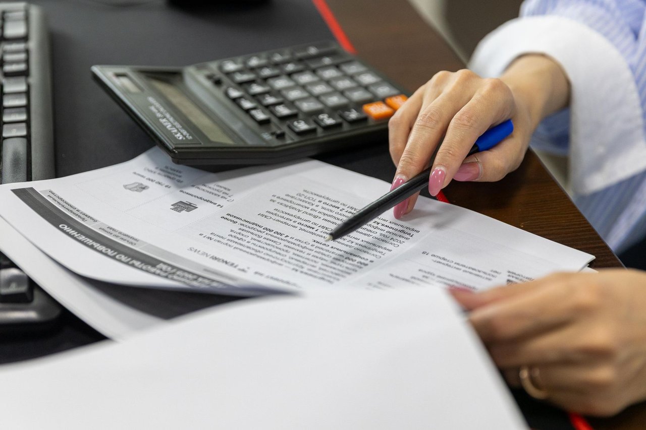 Mão de uma mulher analisando documentos financeiros ao lado de uma calculadora.