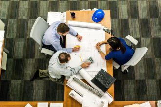 Equipe reunida analisando plantas e documentos de um projeto de construção sobre uma mesa